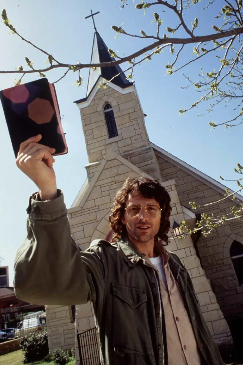 El actor estadounidense Tim Daly (como el líder de la rama davidiana David Koresh) sostiene una Biblia frente a una iglesia en el set de la película para televisión ”En la línea de fuego: Emboscada en Waco” de 1993