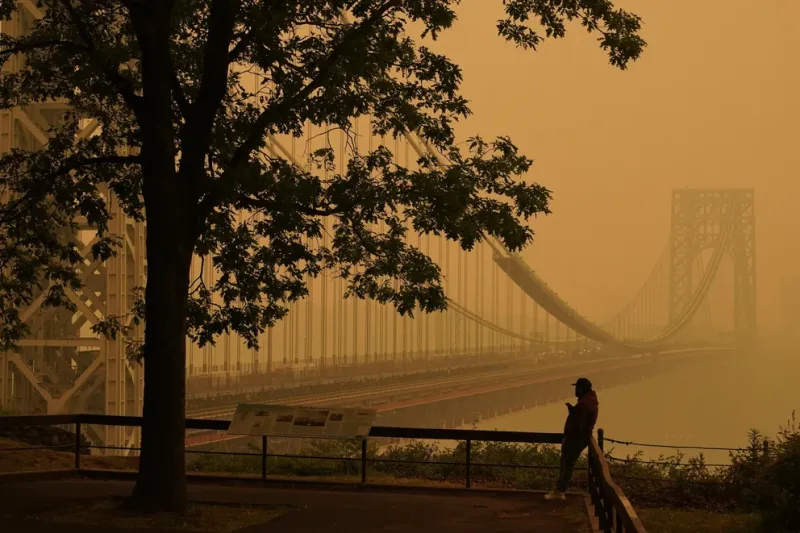 ARCHIVO: un hombre habla por teléfono mientras la neblina cubre el puente George Washington en Fort Lee, Nueva Jersey, el 7 de junio de 2023. El verano ha venido acompañado de humo y los científicos dicen que probablemente será peor en los próximos años